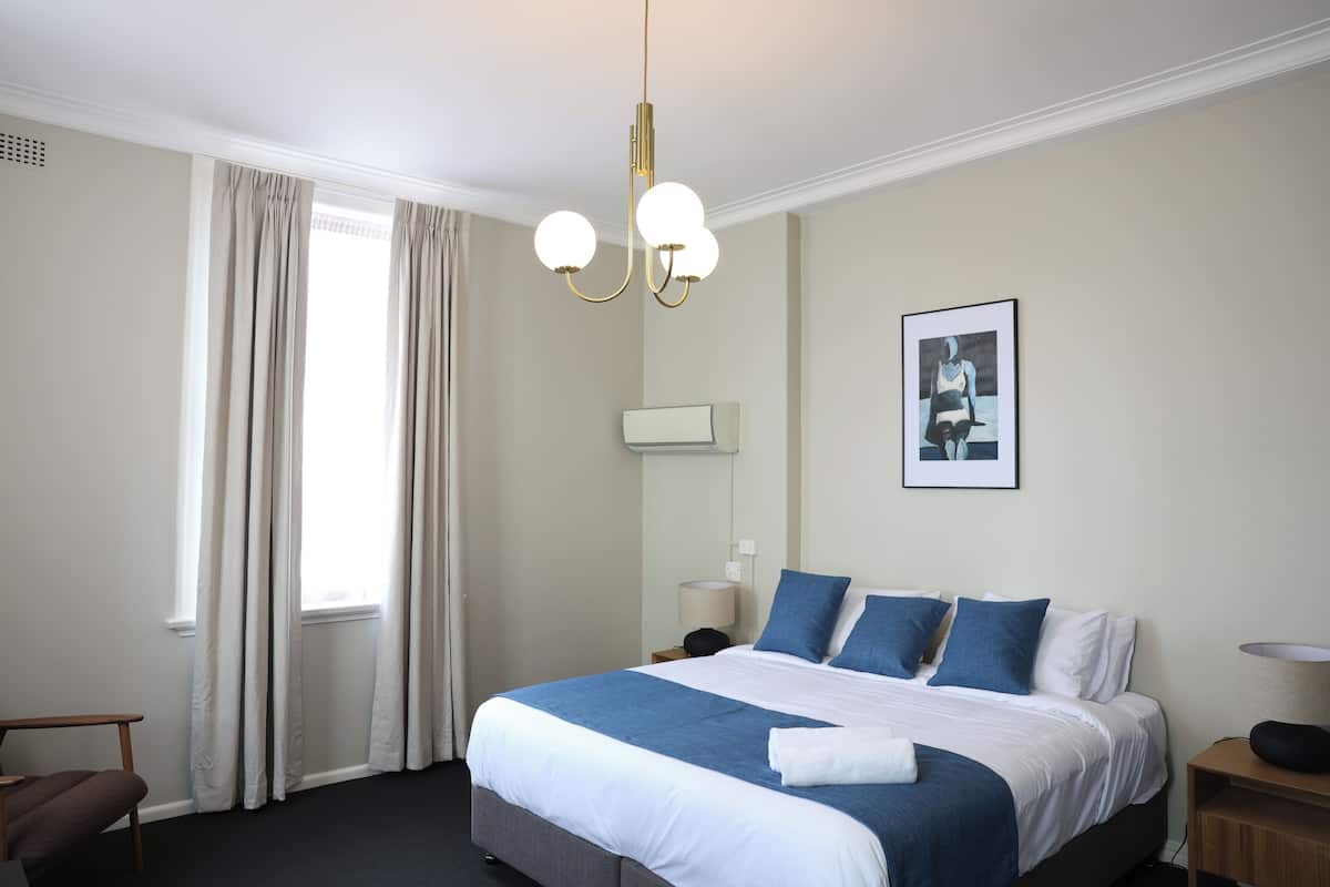 A hotel room with a large bed, a desk, a chair, a lamp, and a picture on the wall.
