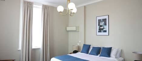Quarto de hotel com uma cama grande, uma escrivaninha, uma cadeira, um abajur e um quadro na parede.
