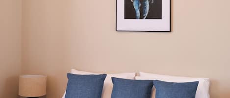 A neatly made bed with blue and white bedding, a framed artwork on the wall, and a bedside lamp.
