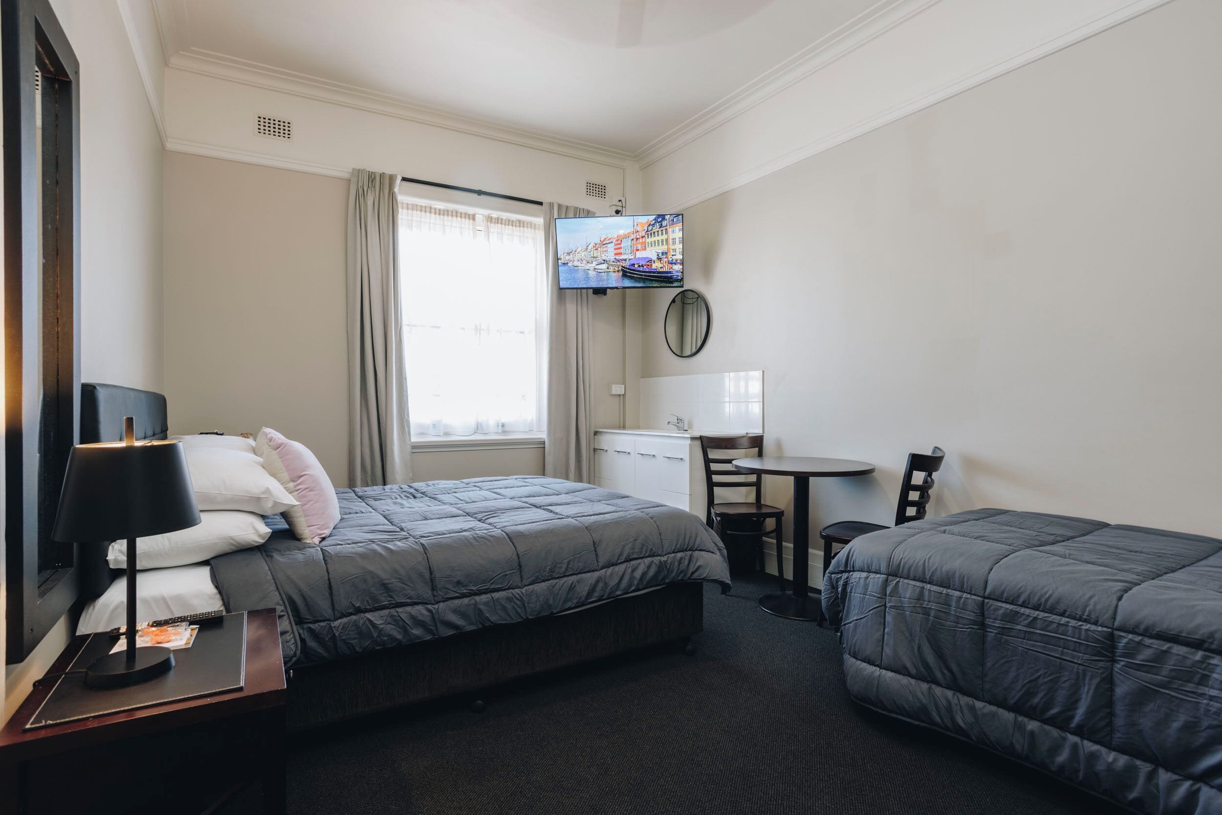 Habitación de hotel con dos camas, un escritorio, una silla, un televisor y una ventana con cortinas.