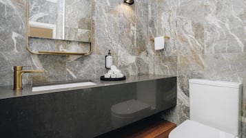 Un baño moderno con salpicadero de mármol, grifo dorado, lavabo negro, inodoro y espejo con marco dorado.