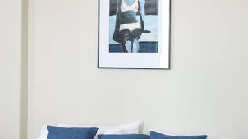 Una cama bien tendida con ropa de cama azul y blanca, un cuadro en la pared y una lámpara sencilla.