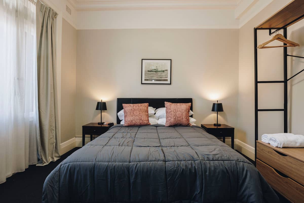 A neatly made bed with a dark blue quilt, two matching pillows, and two bedside lamps.