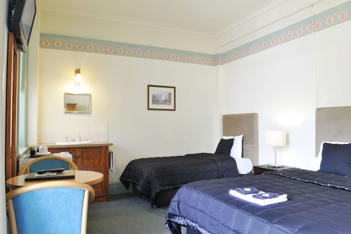A hotel room with two beds, a desk with a chair, a small table, a mirror, and a picture on the wall.