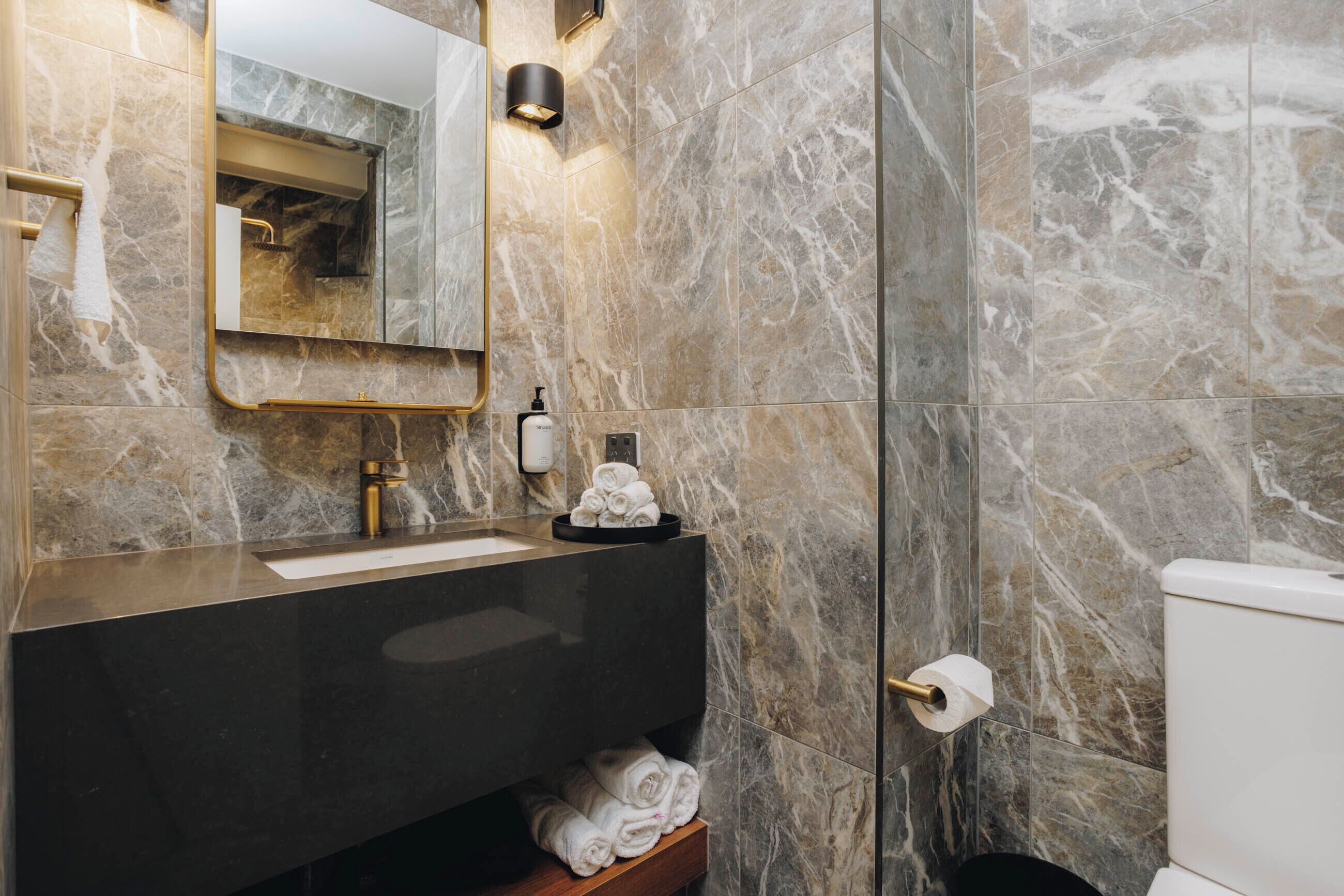 Un baño con paredes de mármol, un lavamanos negro, un espejo y un inodoro.