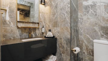 Un baño con paredes de mármol, un lavamanos negro, un espejo y un inodoro.
