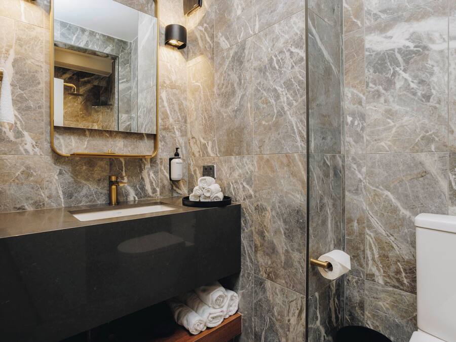Un baño con paredes de mármol, un lavamanos negro, un espejo y un inodoro.