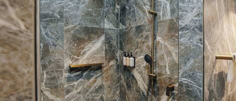 A modern bathroom with a marble shower enclosure, gold fixtures, and a built-in shelf with toiletries.