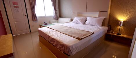 Habitación de hotel con una cama grande, una mesita de noche, cortinas en una ventana y una lámpara de pared.