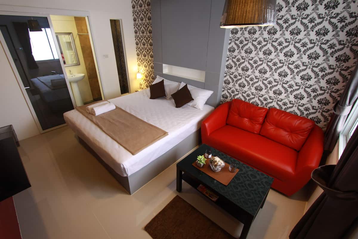 A modern hotel room with a bed, a red sofa, a small table, and a bathroom visible through an open door.