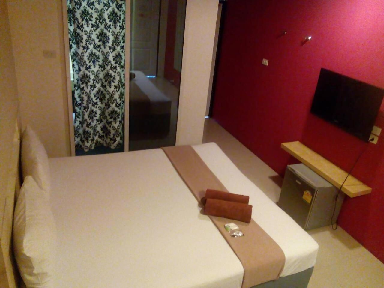 A hotel room with a bed, a small desk, a television, and a red wall.