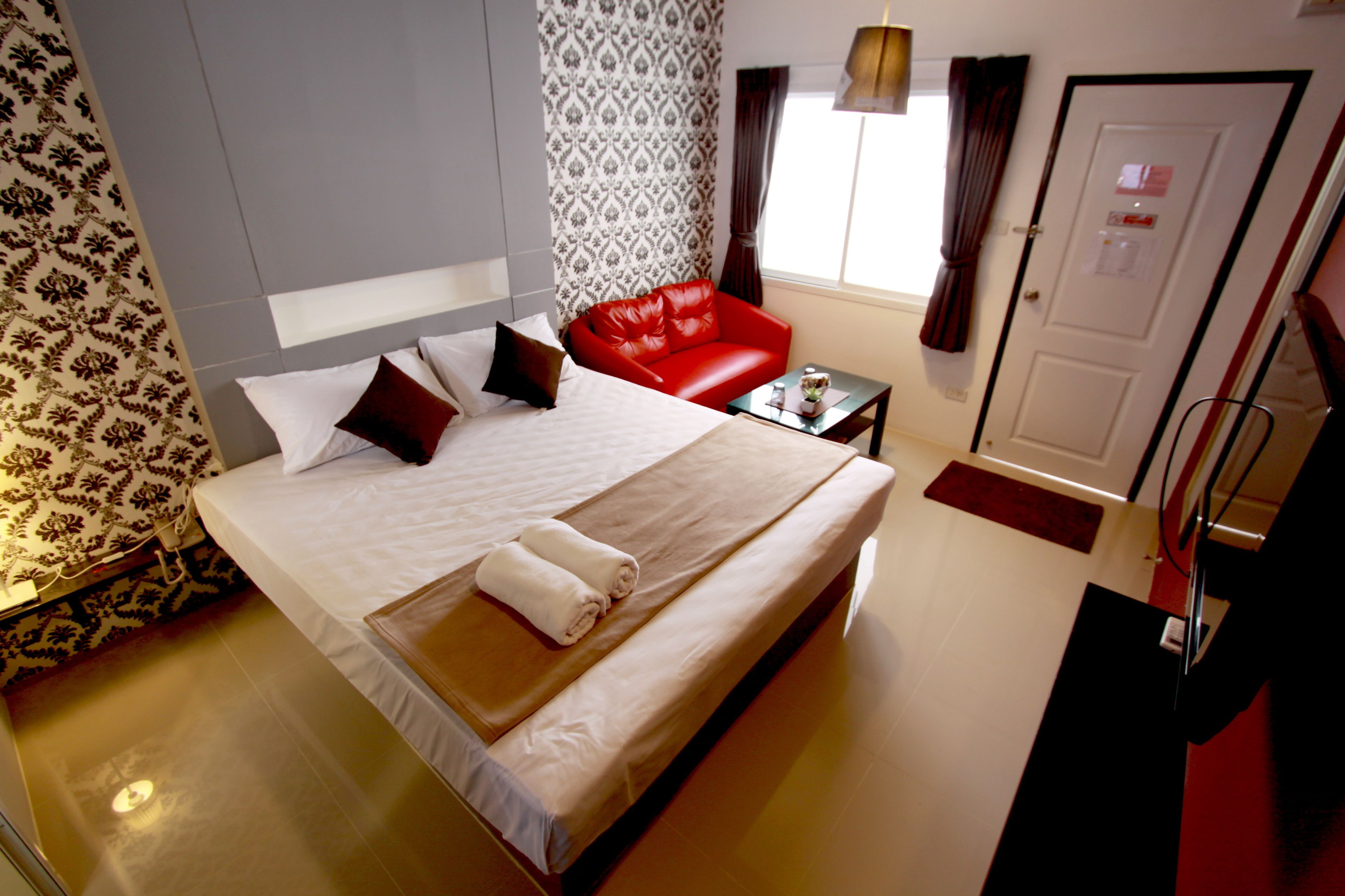 A hotel room with a large bed, a red leather chair, a small table, and a door.