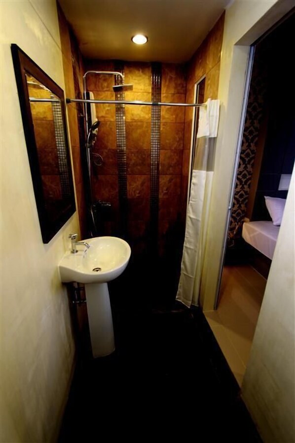 Un baño estrecho con lavamanos blanco, ducha y espejo.