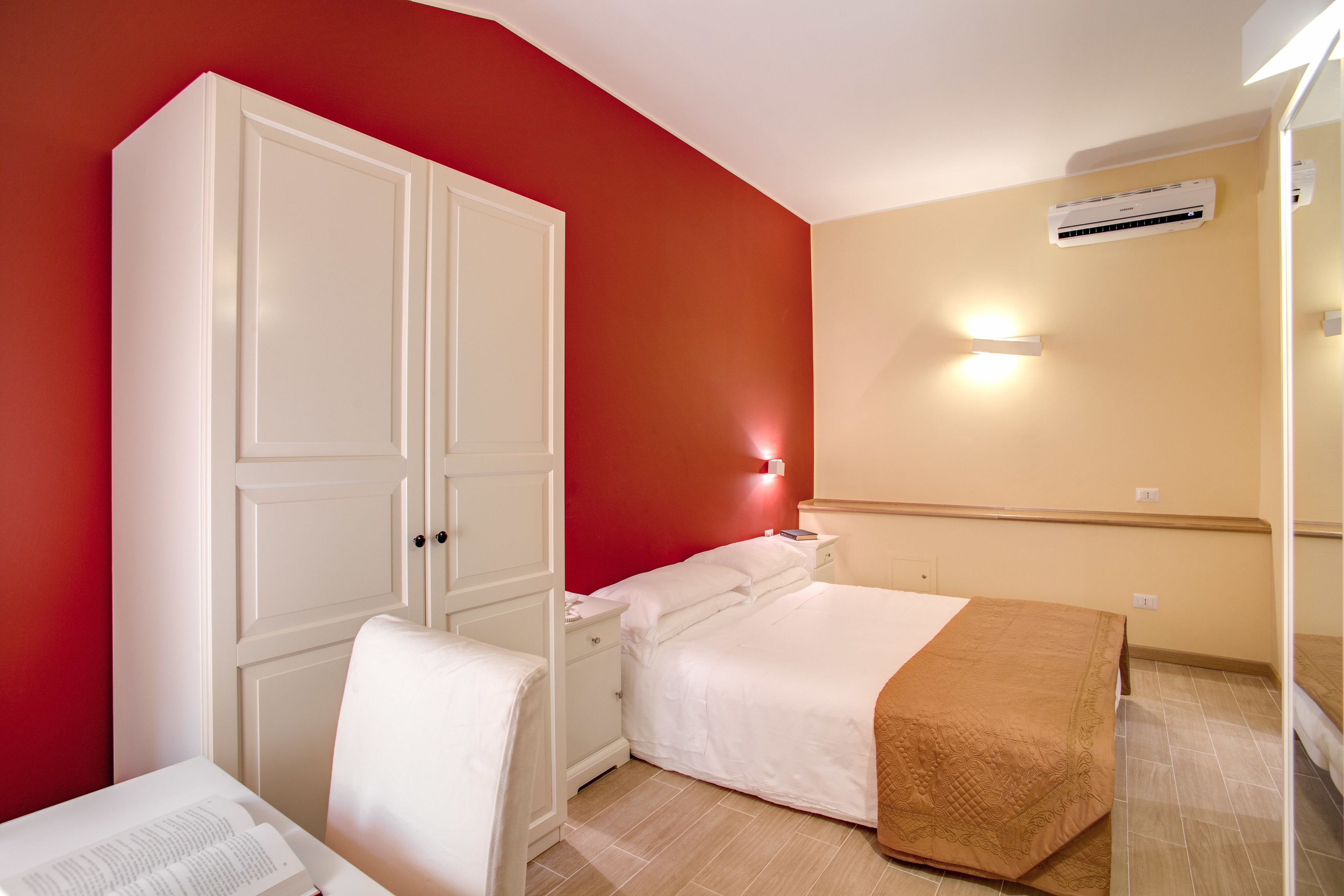 Un dormitorio con una pared roja, un armario blanco, una cama con manta marrón y un equipo de aire acondicionado.