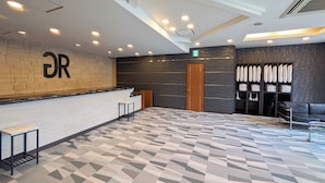 A modern reception area with a marble reception desk, a geometric patterned floor, and a seating area with a black leather couch. - GR Hotel Ginzadori (Kumamoto)