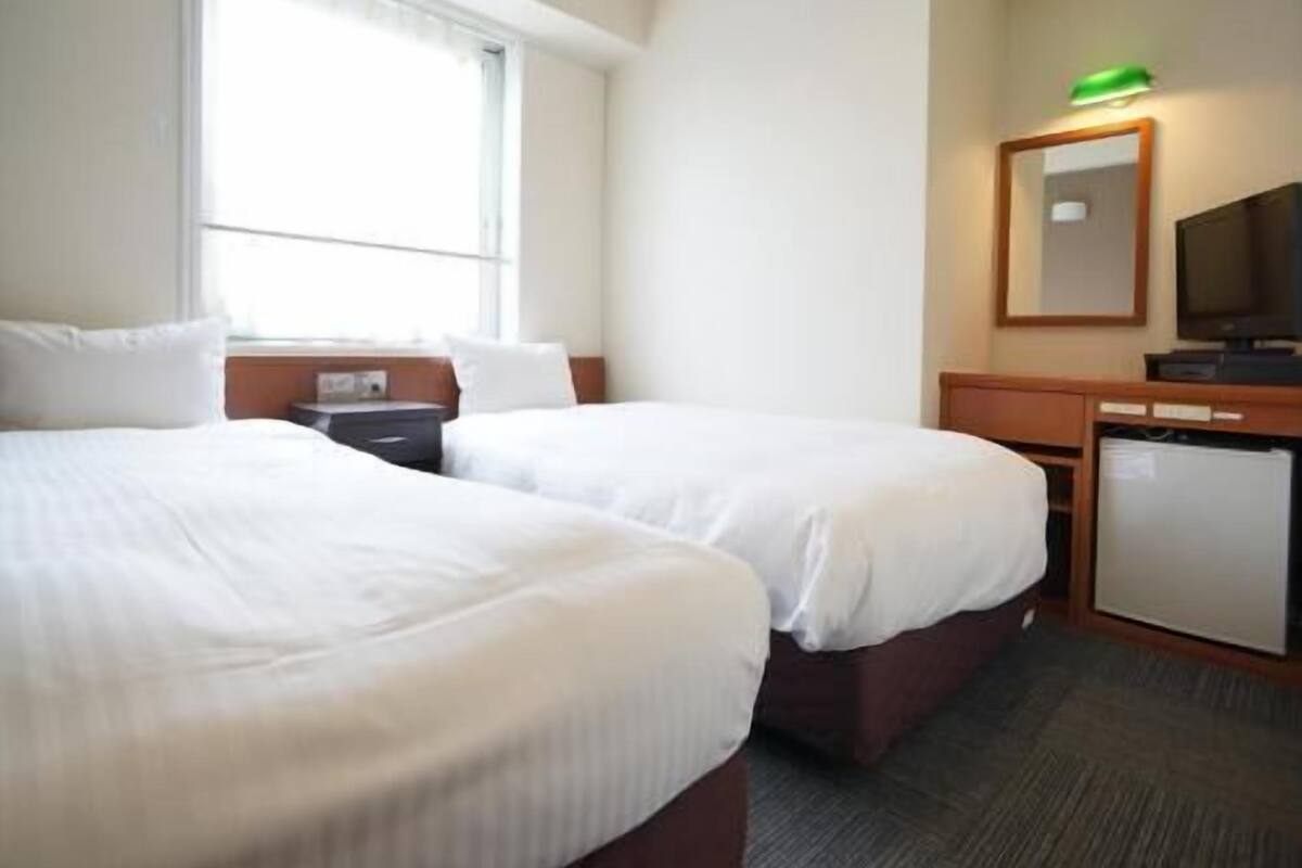 Een hotelkamer met twee bedden, een bureau, een televisie en een kleine koelkast.