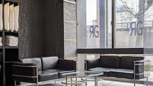 A modern lounge area with black leather sofas, a glass coffee table, and a shelving unit with folded linens. - GR Hotel Ginzadori (Kumamoto)