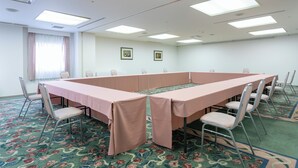 Un salón de conferencias con una larga mesa, sillas y una alfombra estampada.