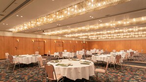 Un salón de conferencias con mesas redondas, manteles blancos y alfombra con motivos florales.