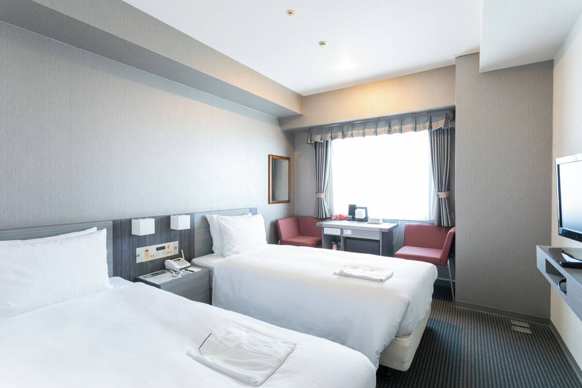A hotel room with two beds, a desk, a chair, a television, and a window with curtains.