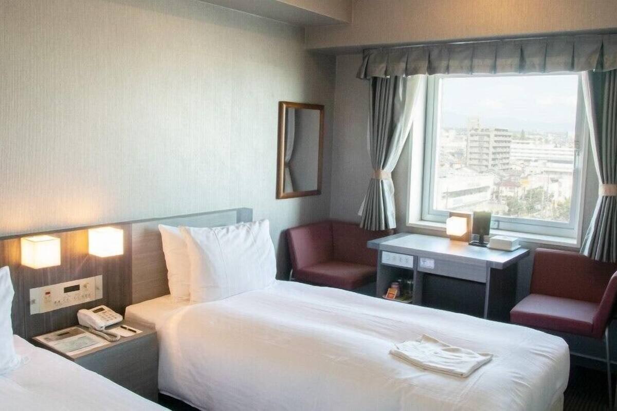 A hotel room with two beds, a desk, a chair, a phone, and a window with curtains.
