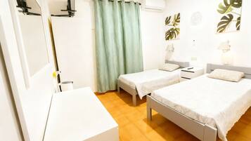 A hotel room with two single beds, a desk, a chair, a wardrobe, a curtain, and wall-mounted artwork.