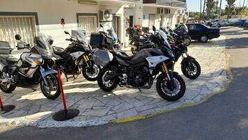A row of parked motorcycles in front of a building with a tiled roof and balconies.