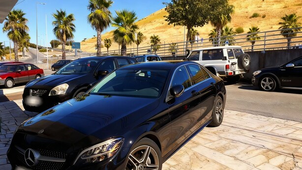 A black Mercedes-Benz parked on a paved area with palm trees and a hilly background. - Residencial Luso Espanhola (Elvas)