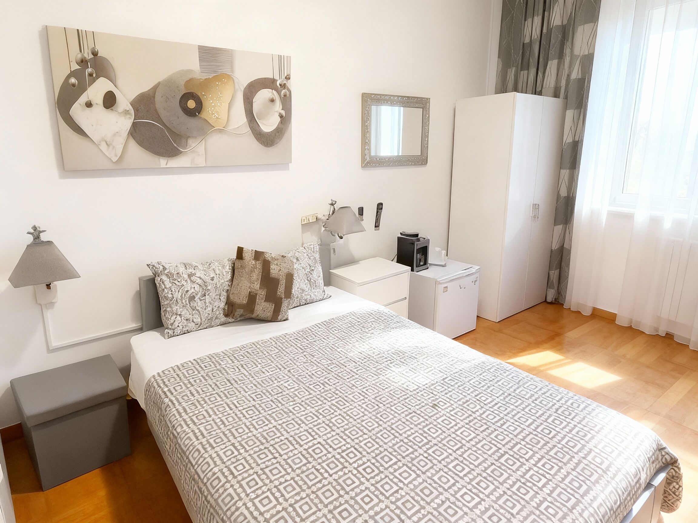 A modern bedroom with a large bed, bedside tables, a wardrobe, a mirror, and a wall art piece.