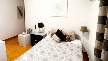 Un dormitorio con cama, mesita de noche, lámpara, reloj de pared y radiador.