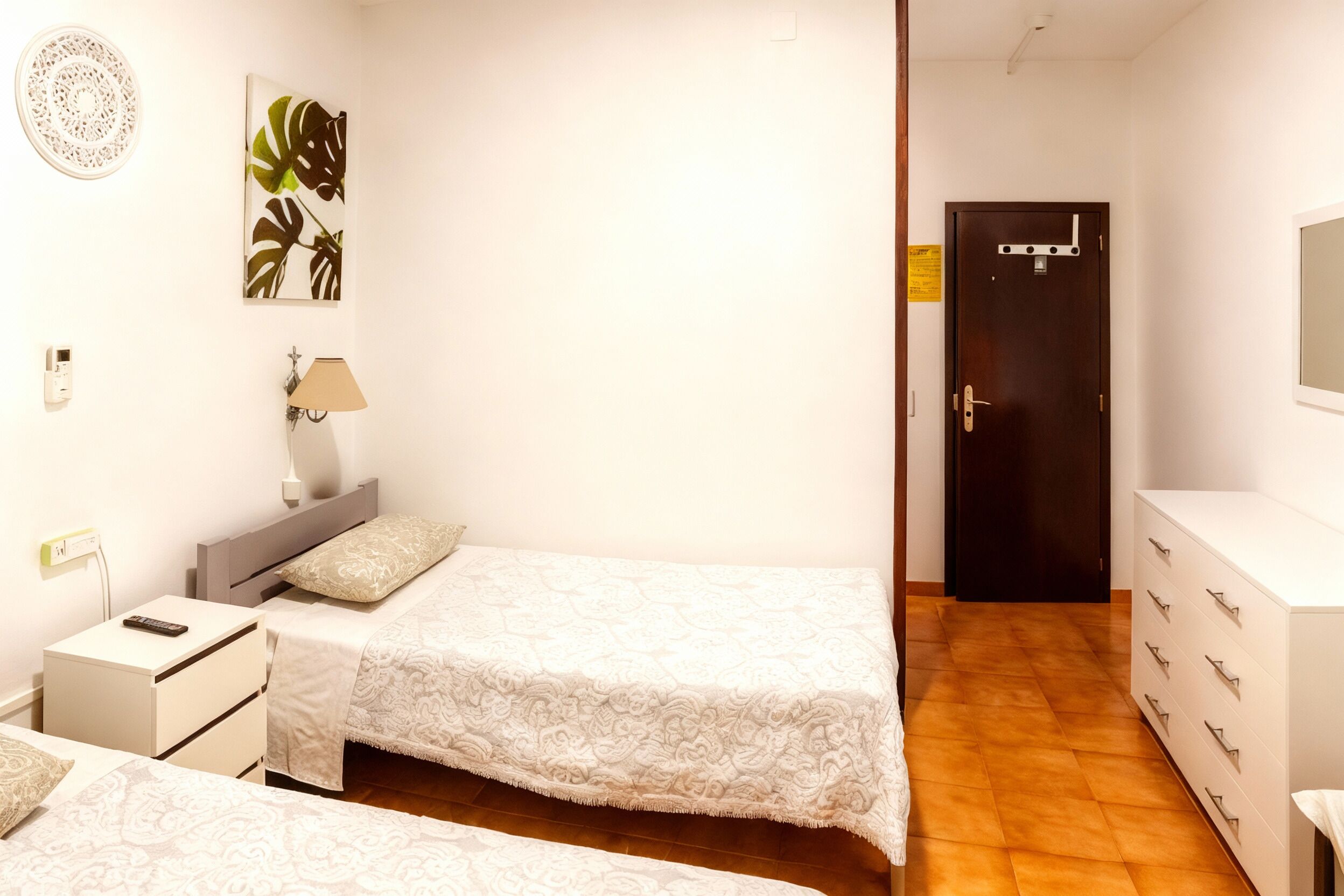 A bedroom with two beds, a nightstand, a lamp, a dresser, and a door.