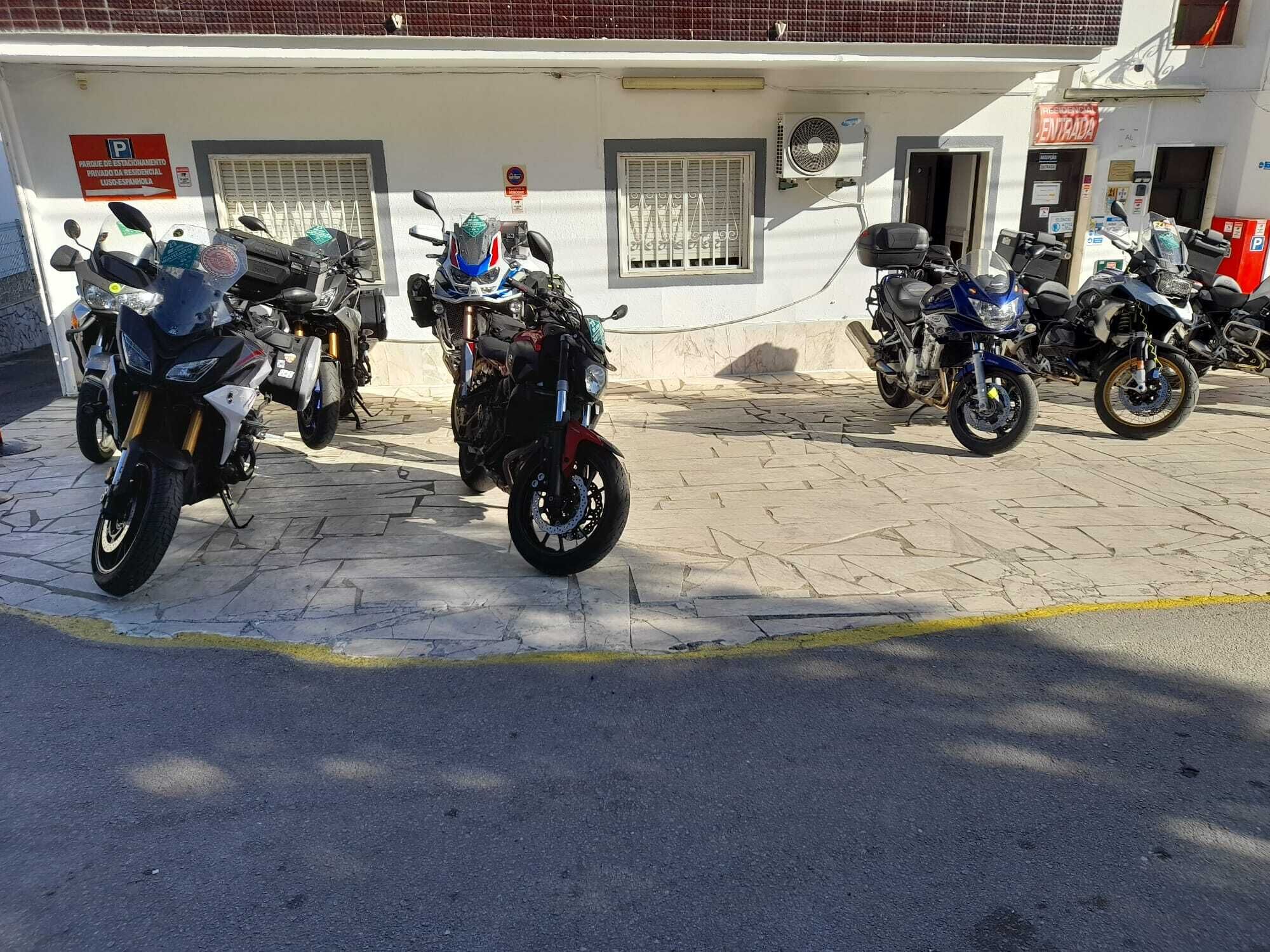 Una fila de motocicletas estacionadas frente a un edificio con un letrero que indica un área de estacionamiento.