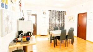A dining area with a table and chairs, a refrigerator, a clock, and a door with a sign. - Residencial Luso Espanhola (Elvas)