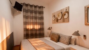 A bedroom with a bed, bedside lamps, a TV mounted on the wall, and a wall-mounted artwork. - Residencial Luso Espanhola (Elvas)