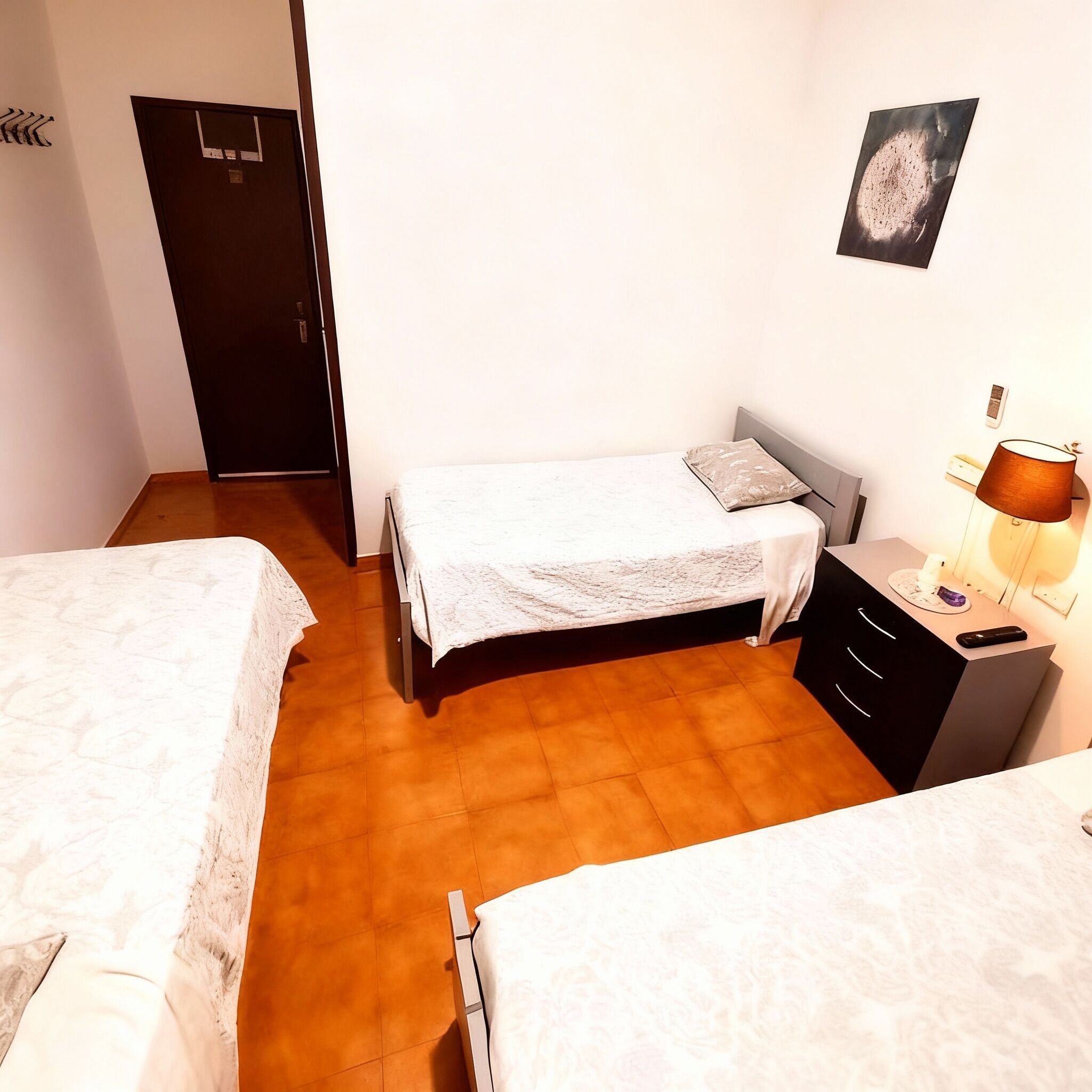 Une chambre avec deux lits, une table de chevet avec une lampe, un tableau accroché au mur et une porte.
