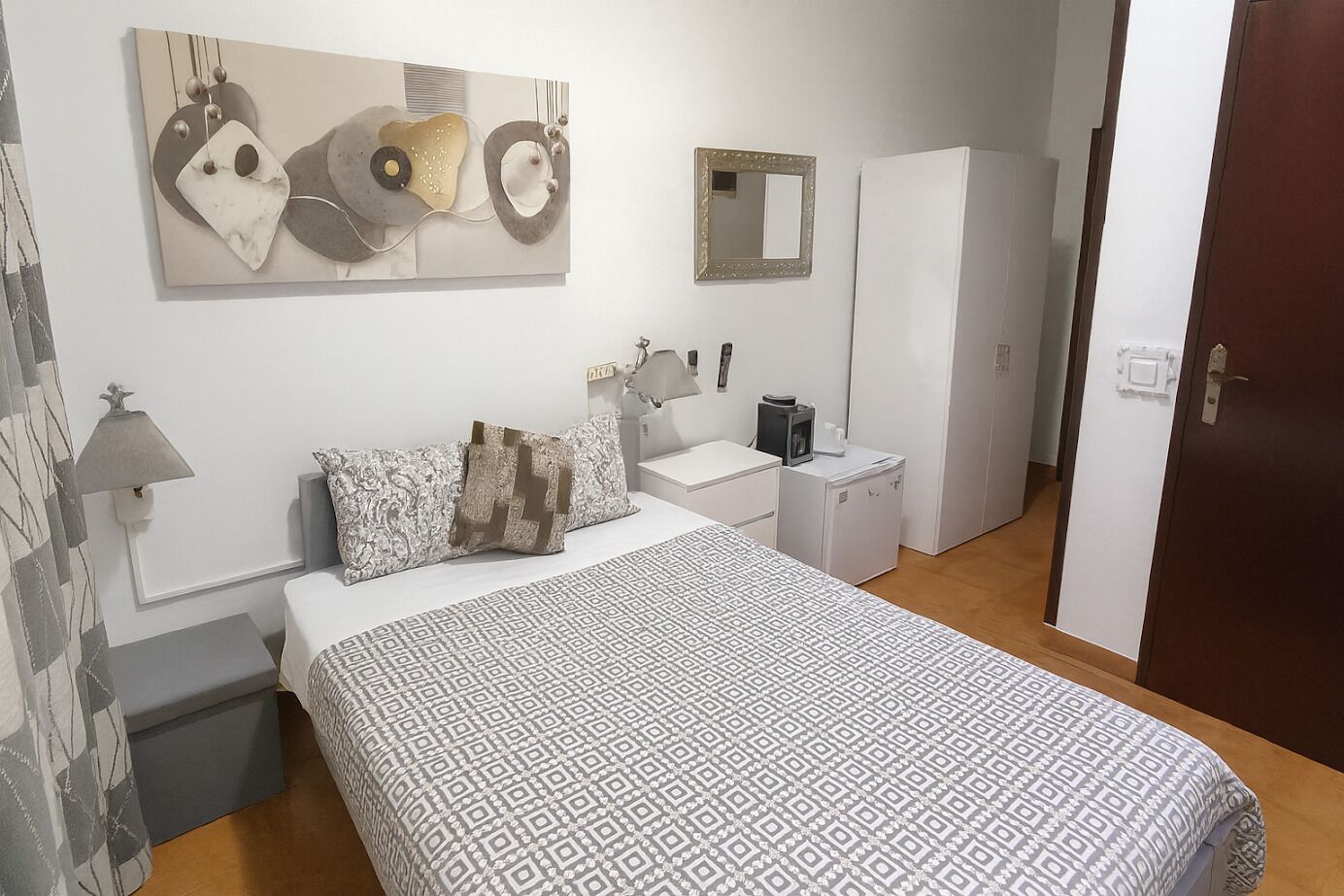 Un dormitorio con cama, dos mesitas de noche, cómoda, espejo y puerta.