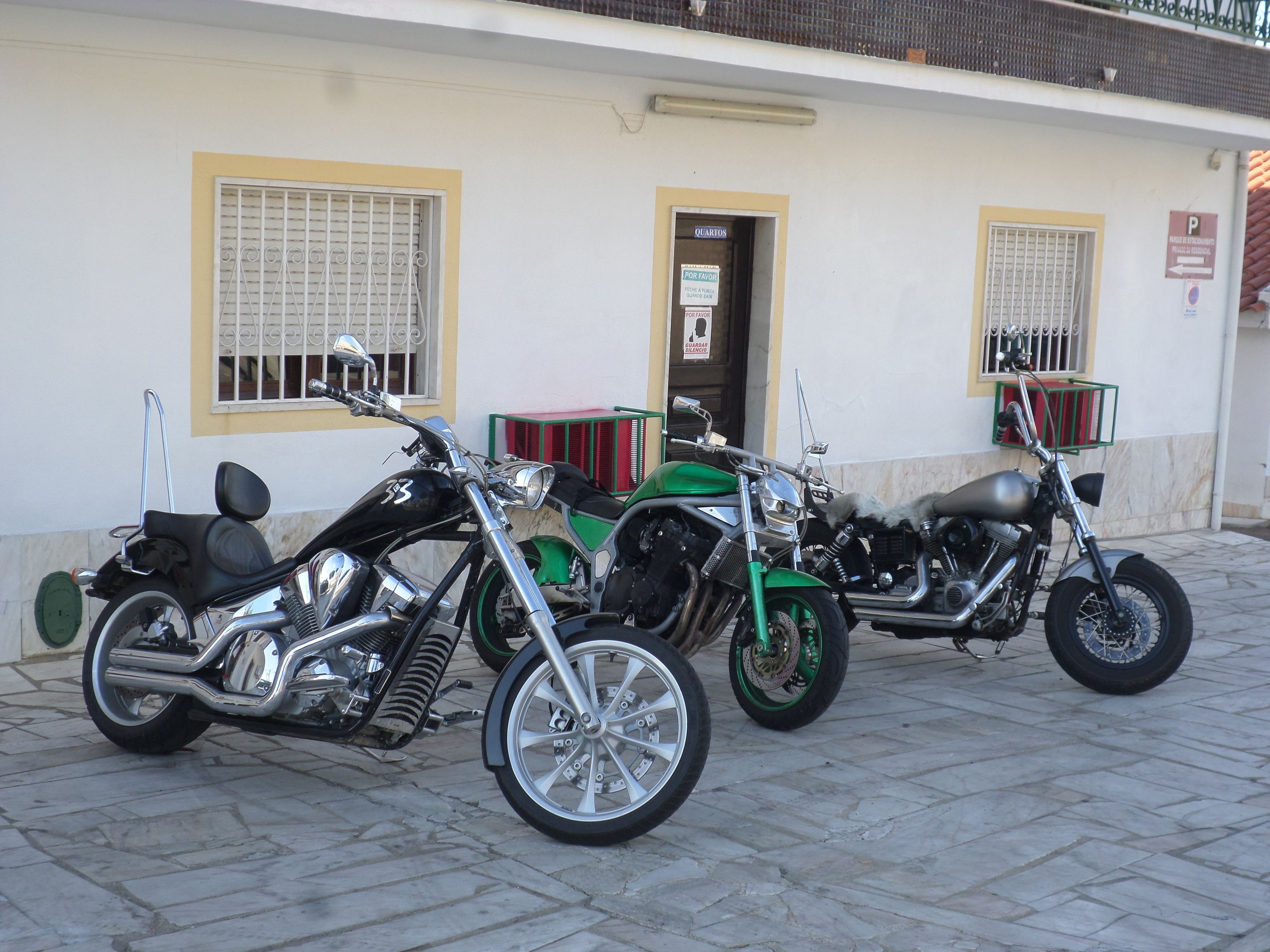 Trois motos sont garées devant un immeuble qui a une porte et des fenêtres.