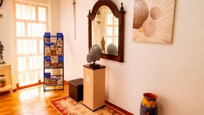 A room with a wooden floor, a red floral rug, a small table with a decorative item, a tall cabinet, a mirror, and a vase. - Residencial Luso Espanhola (Elvas)