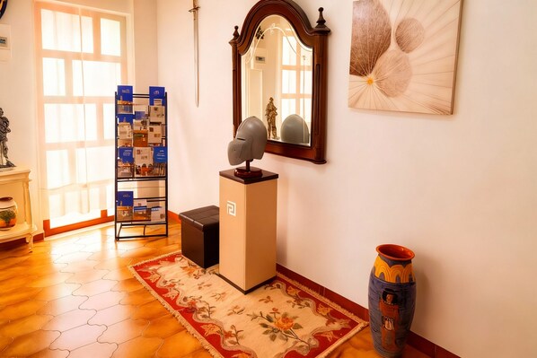 A room with a wooden floor, a red floral rug, a small table with a decorative item, a tall cabinet, a mirror, and a vase.