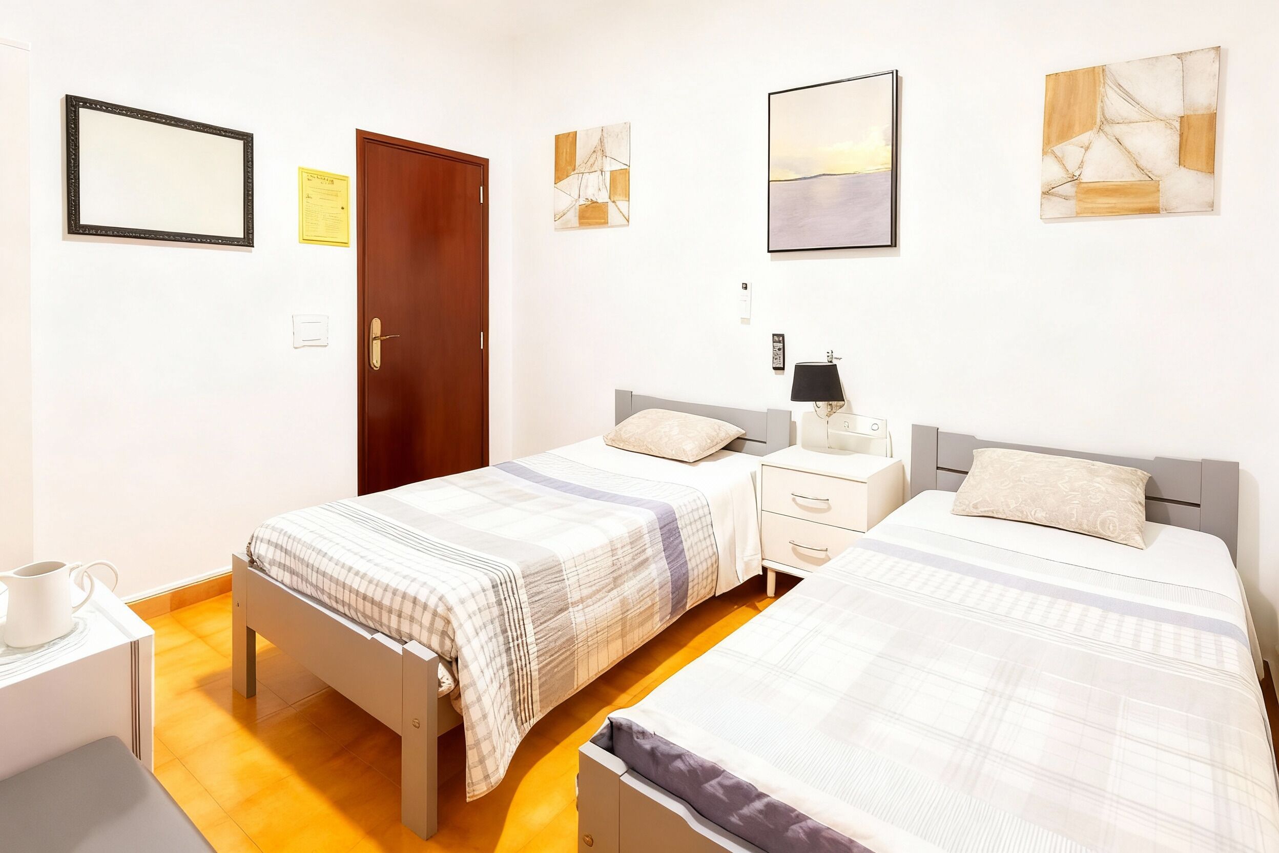 Un dormitorio con dos camas, una mesita de noche con lámpara, una mesita auxiliar y un interruptor de luz en la pared.