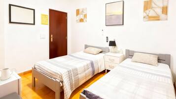 Un dormitorio con dos camas, una mesita de noche con lámpara, una mesita auxiliar y un interruptor de luz en la pared.
