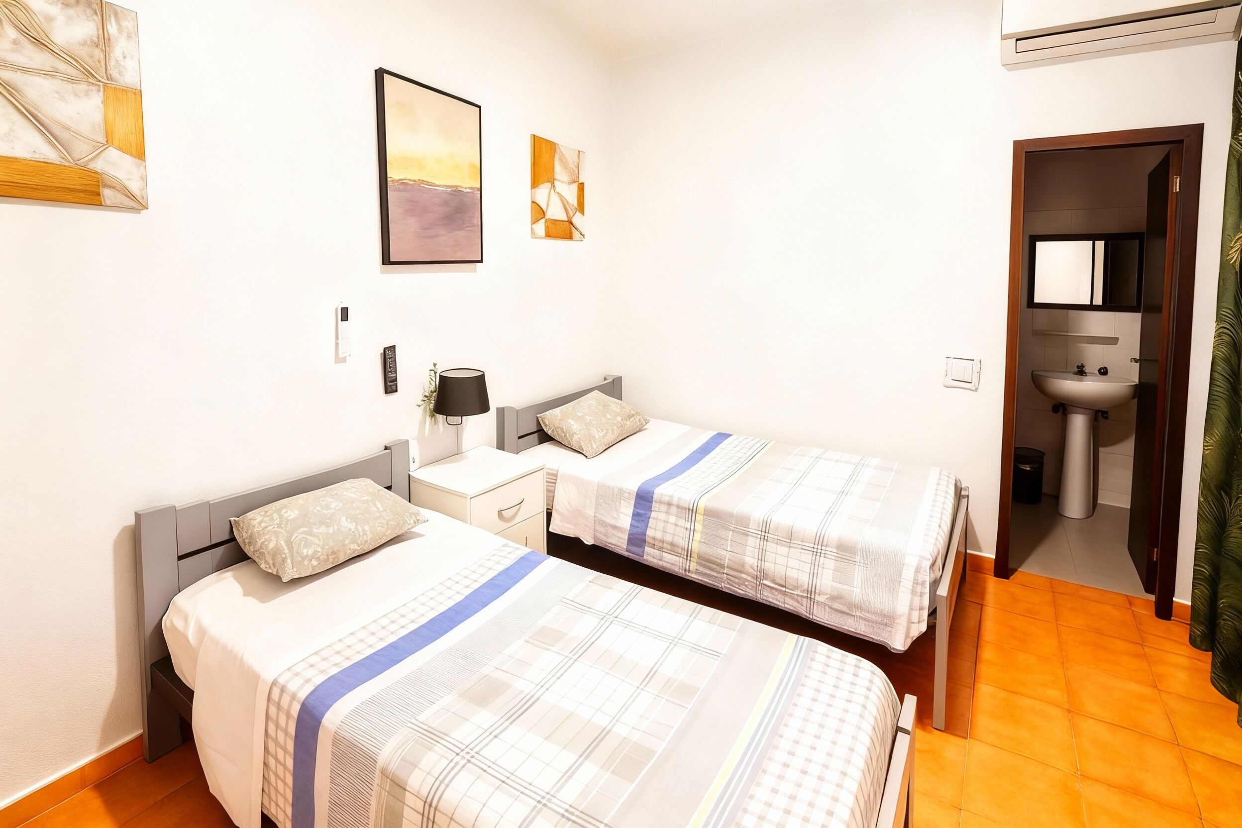 A bedroom with two beds, a nightstand, a lamp, and a painting on the wall.