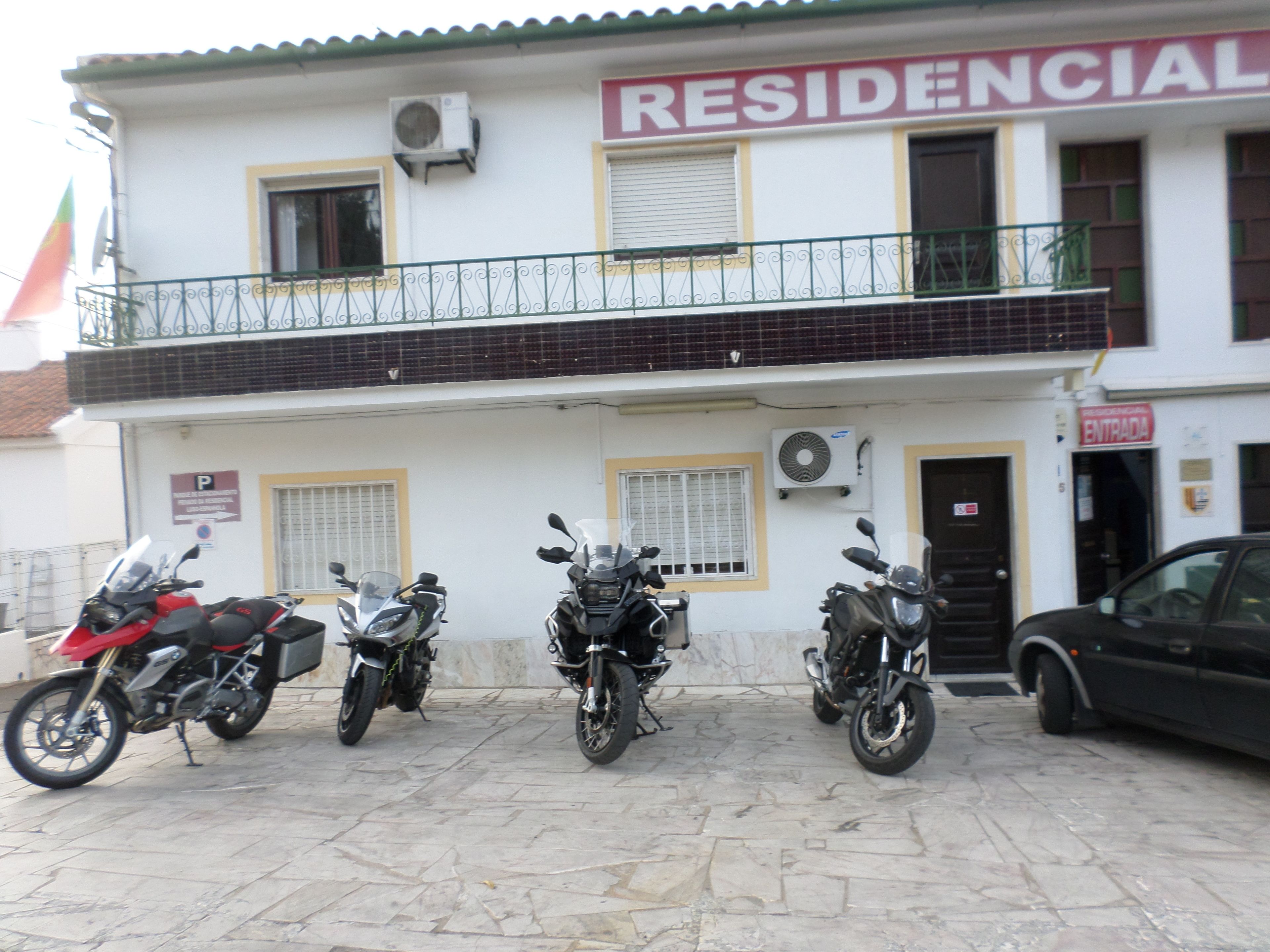 Un edificio residencial con un letrero que dice "RESIDENCIAL" y un cartel de estacionamiento con la letra "P". Cuatro motocicletas estacionadas al frente.