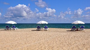 Une plage avec des parasols blancs et des chaises longues bleues disposées sur le sable.