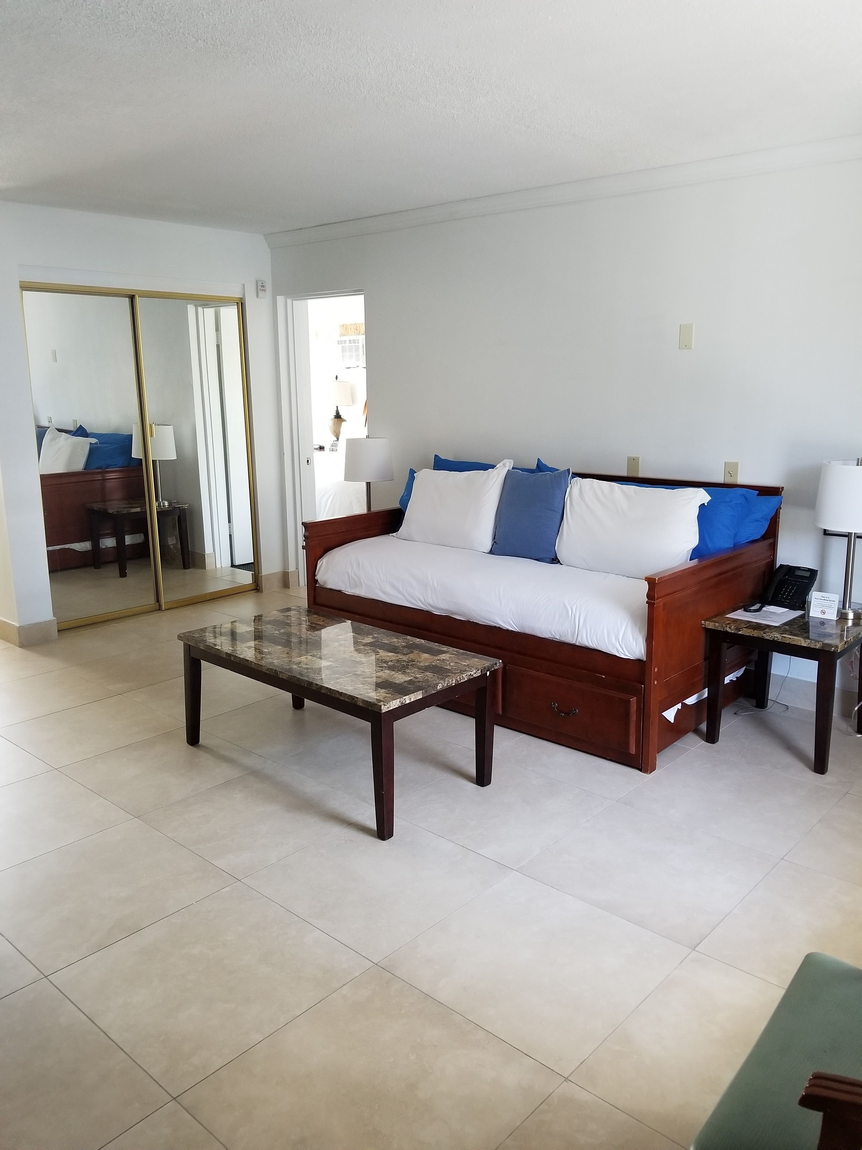 Una habitación de hotel con una cama de madera, una mesita de centro de cristal, un escritorio con lámpara y un espejo grande.