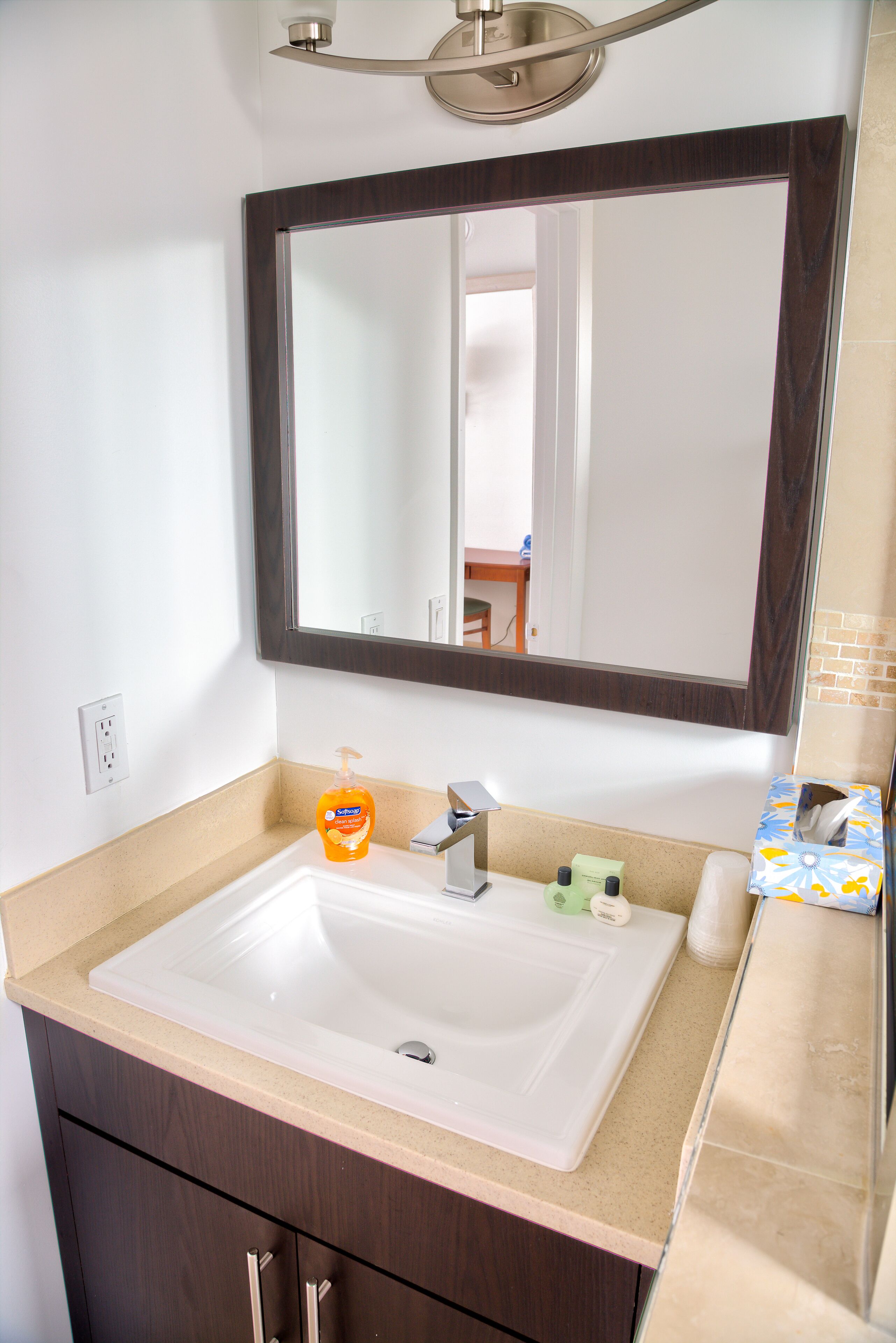 A bathroom with a white sink, dark wooden cabinet, and a large mirror above the sink.