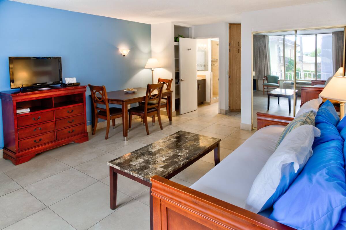 Ein Hotelzimmer mit Bett, einem Holztisch, einem Fernseher, einem Esstisch mit Stühlen und einem durch eine offene Tür einsehbaren Küchenbereich.