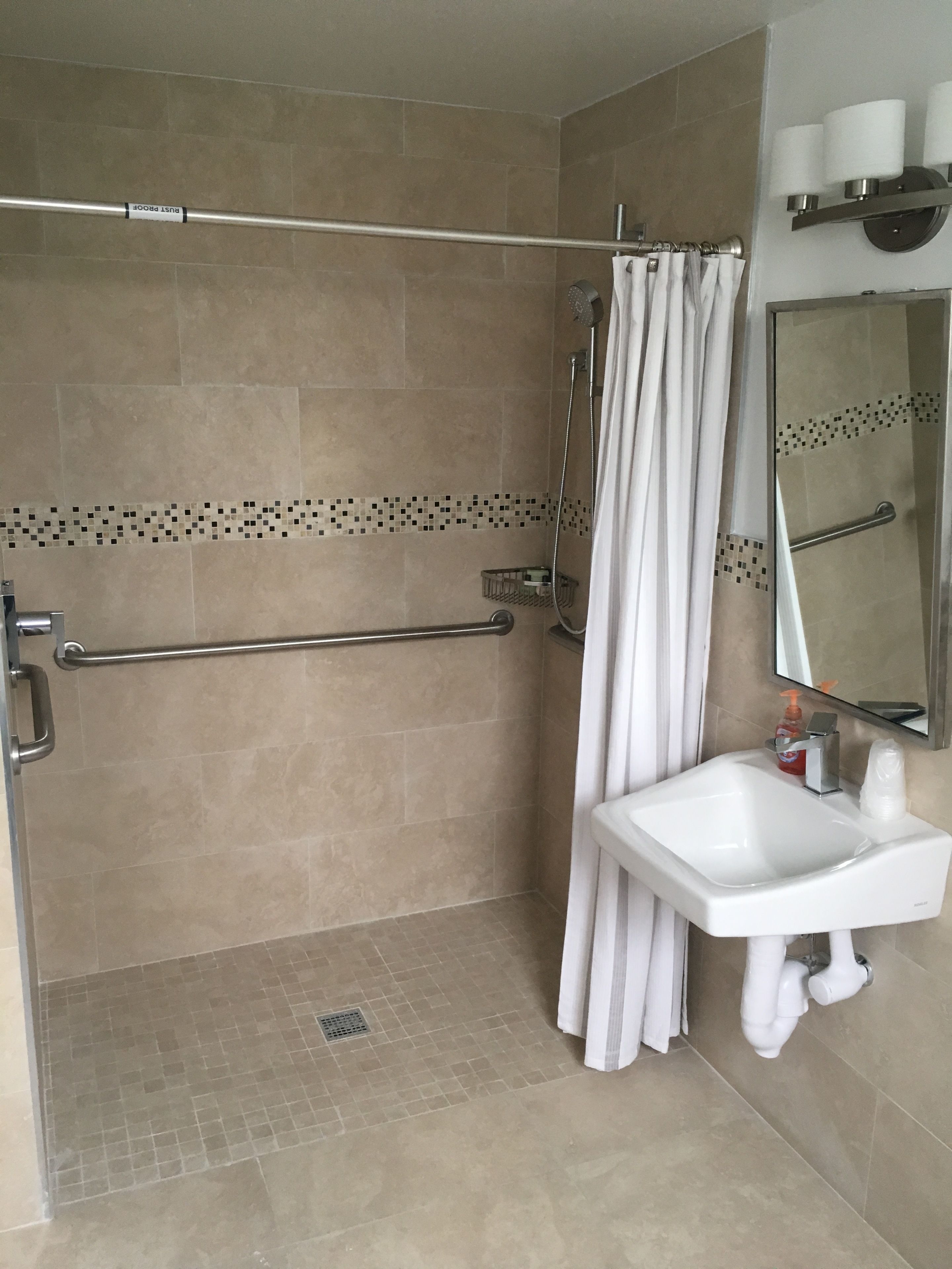 Un baño con ducha, barra de apoyo, lavabo y espejo.