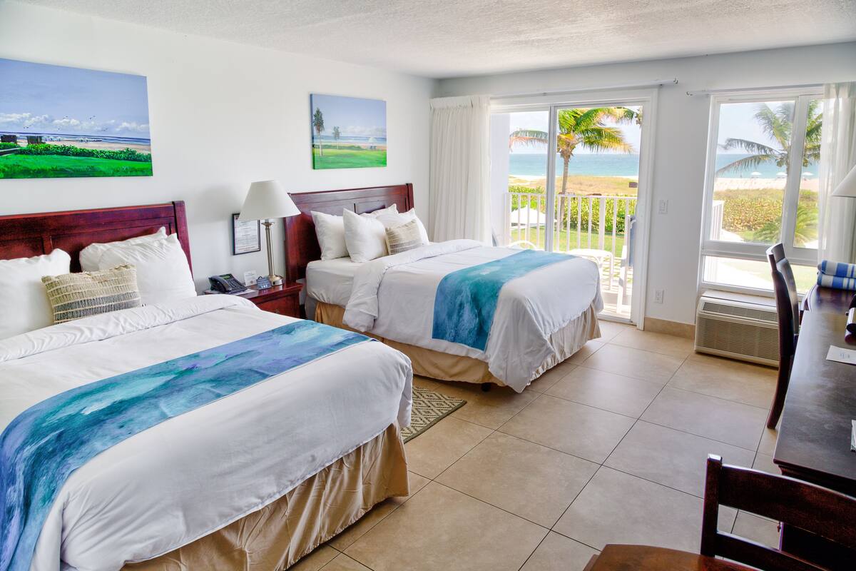 Ein Hotelzimmer mit zwei Betten, einem Esstisch und Blick auf den Strand.