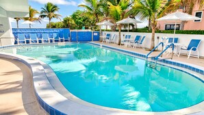 Une piscine aux carreaux bleus, des chaises longues blanches et des palmiers.